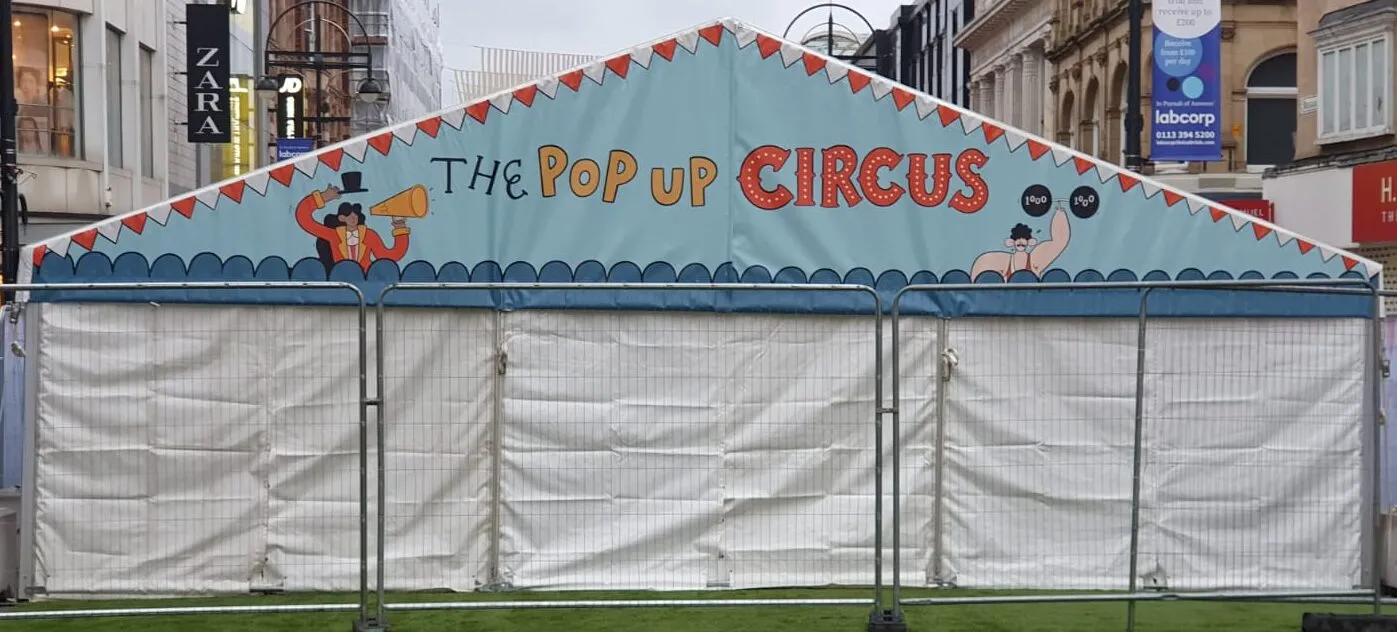 A marquee gable printed with a design, standing on a paved street behind temporary fencing